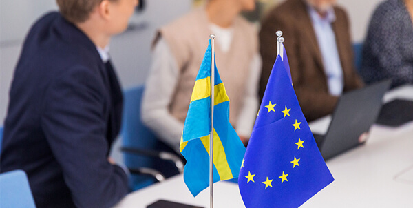 Svenska flaggan och EU-flaggan med människor i bakgrunden.